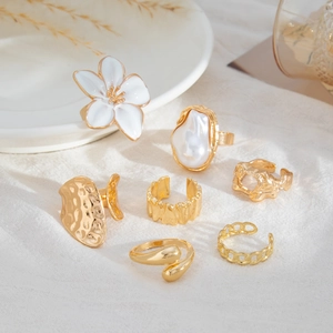 Detailopname van een zevendelige gouden ringenset met barokparel en florale bedeltjes