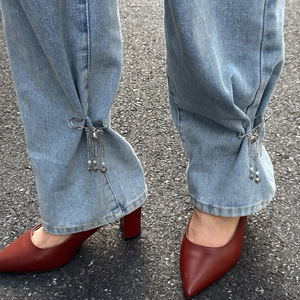 Nahaufnahme von Jeanssaum mit Herz- und Perlen-Anstecker sowie roten hohen Schuhen