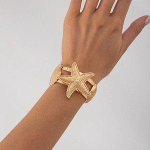 Detail einer goldenen Armspange mit strukturiertem Seestern und Muschel am Handgelenk
