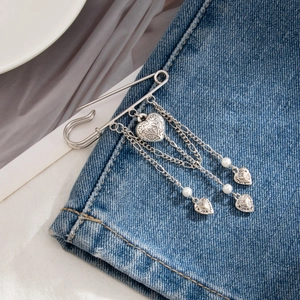 Detail of silver heart tassel brooch pin with pearls on navy denim fabric background