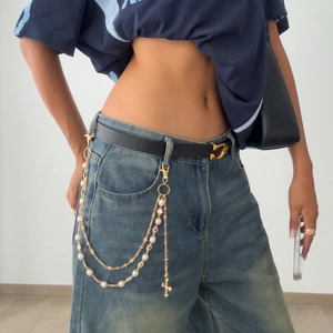 Detail of layered gold metal waist chain with pearls and cross charms on denim