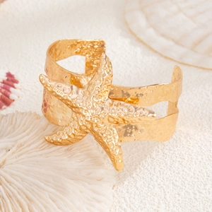 Makro-Detail des goldenen Seestern-Armreifs mit strukturierter Oberfläche und Muschel-Deko