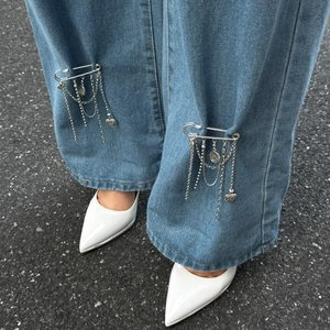 Detail einer silbernen Herz-Quasten-Brosche auf blauen Jeans mit weißen High Heels