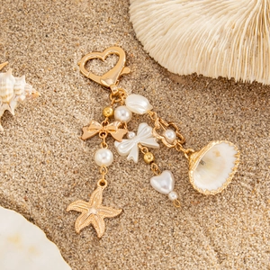 Ocean-themed keychain with gold heart clasp, seashell, and pearl charms on sandy beach
