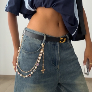 Detail of multilayer gold pants chain with colored crystals, pearls, and cross charms