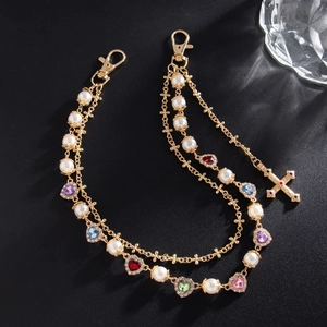 Detail of gold multilayer pants chain with faux pearls, colorful hearts and crystal cross