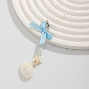 Detail of seashell and starfish pendant with blue ribbon bow on a white textured tray