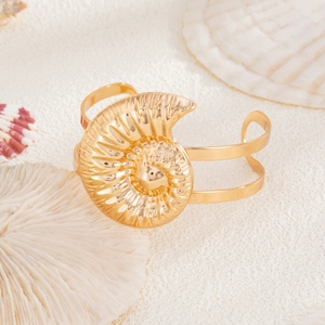 Detailansicht eines goldenen Muschelarmbands mit Nautilus-Struktur auf weißem Sand