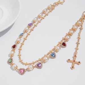 Detail of multilayered gold chain with colorful rhinestone hearts and pearl cross charm