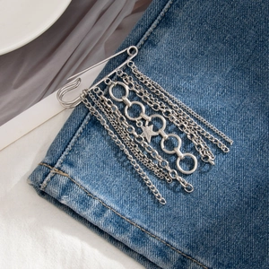 Silver punk safety pin brooch with star charm and tassel chains on blue denim fabric