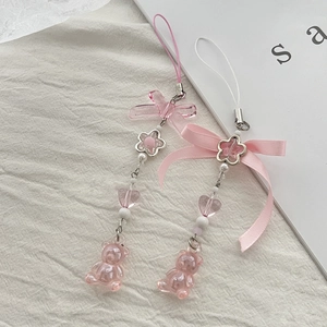 Close-up of pink resin bear and bowknot charms with heart beads on white linen
