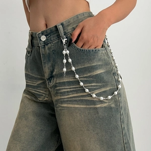 Detail of layered silver pants chain with white pearls and cross charm on denim jeans