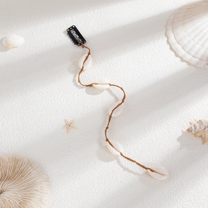 Détail d'une pince à cheveux avec coquillages cauris sur fond de plage de sable