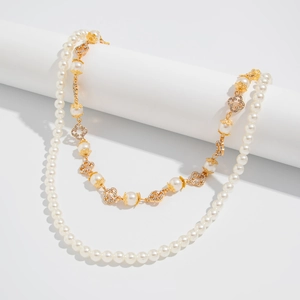 Detail of layered gold necklace featuring faux pearls and sparkling clover motifs on white props