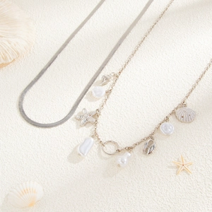 Detail of silver layered necklace with seashell, starfish charms and pearls on a stone base