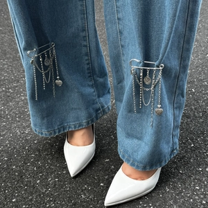 Sicherheitsnadel-Brosche mit Herz- und Münzanhängern an einer Jeans-Manschette