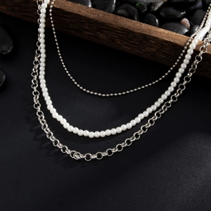 Détail du collier superposé avec perles blanches et pendentif croix en métal argenté