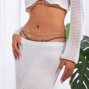Close-up of golden waist chain with starfish and shell charms over crochet clothing