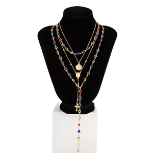 Dettaglio di una collana dorata a strati con cristalli colorati e ciondolo a croce su busto