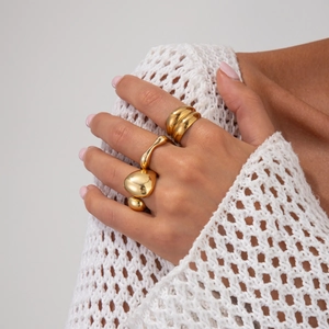 Détail de bagues gouttes dorées minimalistes sur main avec fond en maille crochet blanc