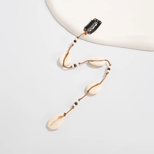 Détail d'une pince à cheveux bohème avec coquillages, perles et pompons de plage
