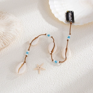 Détail de pince à cheveux avec coquillages naturels et perles bleues sur sable blanc