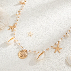 Detail of gold starfish and shell charms with white pearls on a beach style body chain
