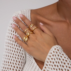 Détail d'un ensemble de cinq bagues dorées porté avec un pull en maille blanc
