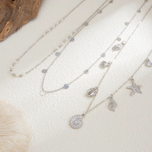 Detailed view of silver nautical charm necklaces with starfish, shells and white pearls