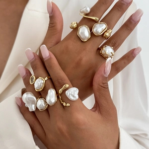 Detailed view of layered golden rings with baroque pearls on a white blazer background