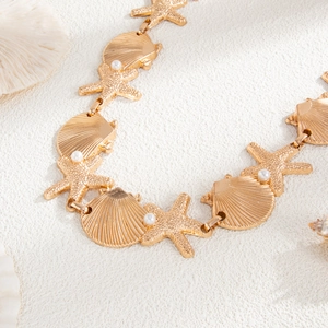 Detail of golden starfish and seashell body chain with white pearls on a beach setting