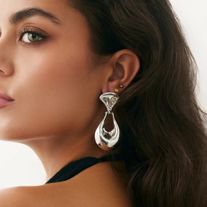Close-up of a model wearing large silver irregular hollow teardrop earrings in metal
