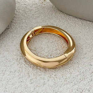 Detailed close-up of chunky gold-plated hinged bracelet with polished mirror finish