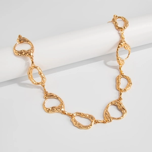 Macro detail of irregular gold metal chain links with liquid lava texture on white pedestal