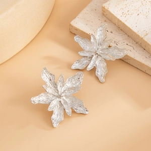 Detailed close-up of large silver floral earrings with organic wrinkled metal texture
