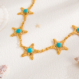 Close-up of golden starfish waist chain with turquoise inlays on white sand