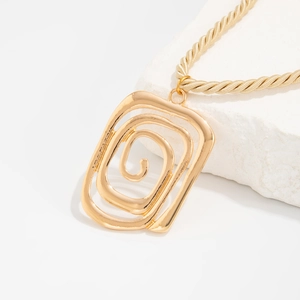 Detail of gold hollow rectangle conch pendant with chunky rope chain on textured stone