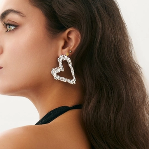 Close-up of liquid lava textured silver heart earrings worn by a model in a side view