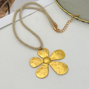 Detail eines mattgoldenen fünfblättrigen Blumenanhängers mit cremefarbener Kordelkette