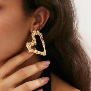 Close-up of a model wearing large hollow gold heart earrings with crumpled metal texture