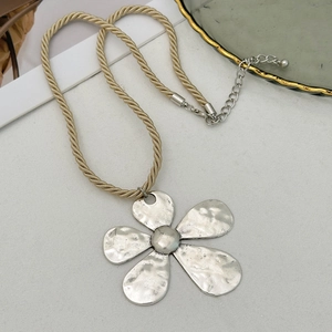 Macro detail of silver hammered flower pendant on a beige twisted rope chain necklace