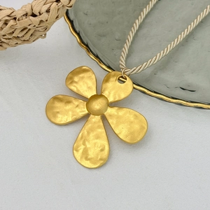 Close-up of matte gold hammered flower pendant with ivory woven cord necklace
