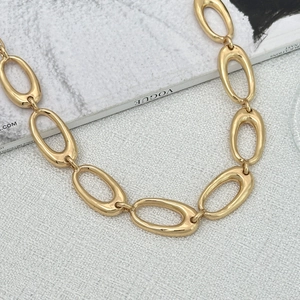 Close-up of golden chunky oval link chain necklace with polished finish on white fabric