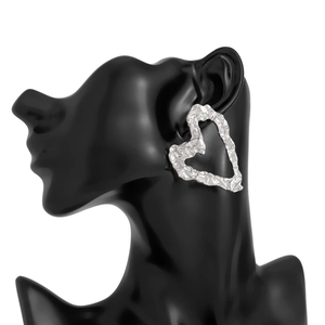 Detailed view of silver heart earrings with irregular hammered texture on a model