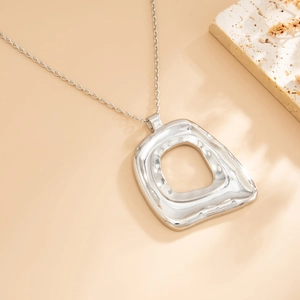 Macro detail of irregular hollow square pendant with hammered texture on silver chain