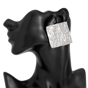Macro view of square silver earrings with hammered texture on a black model silhouette