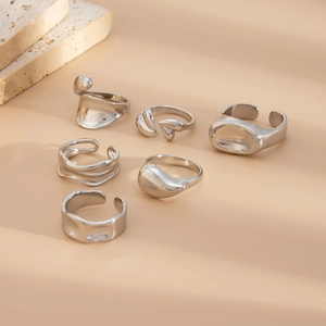 Detail of six silver molten rings on beige stone background with soft shadows