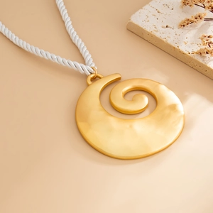 Detail of a large gold spiral shell pendant necklace on white cord with boho decor