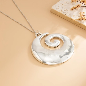 Detail of silver spiral pendant necklace with a hand-hammered texture on sandy surface