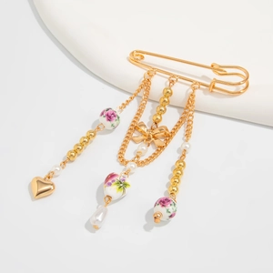 Detail of a vintage golden pin brooch featuring ceramic floral beads and a pearl teardrop